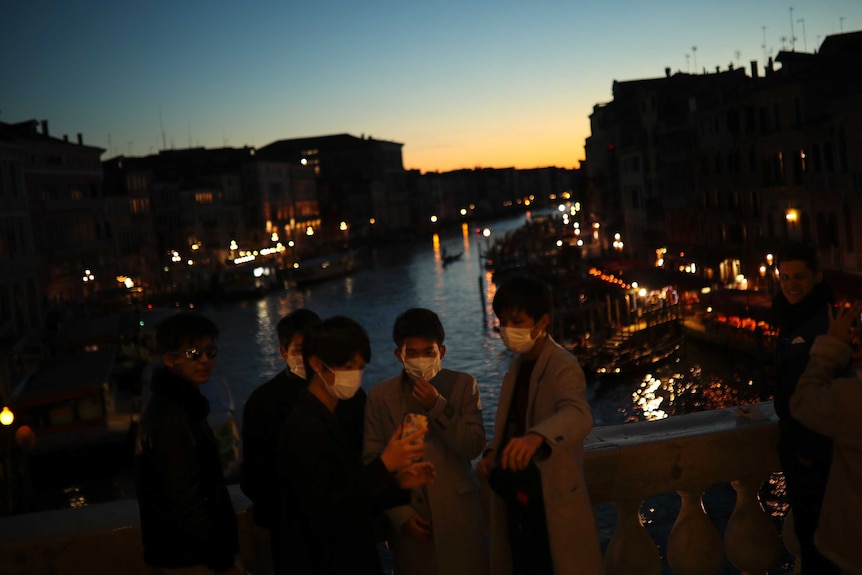 Tourists wearing protective masks pose for a photograph at the Rialto bridge as the sun sets in Venice.