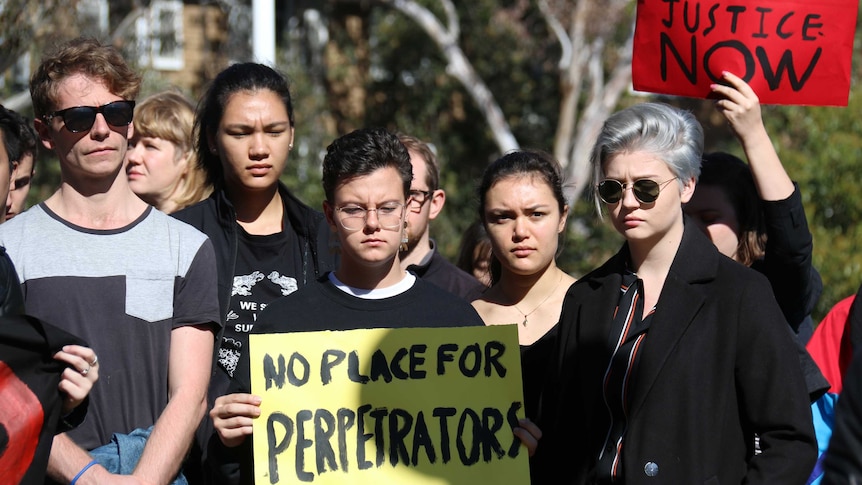 Protesters hold up a sign saying 'No place for perpetrators'.