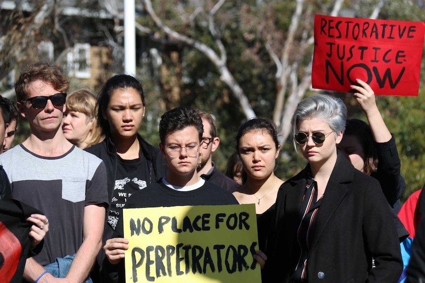 Protesters hold up a sign saying 'No place for perpetrators'.