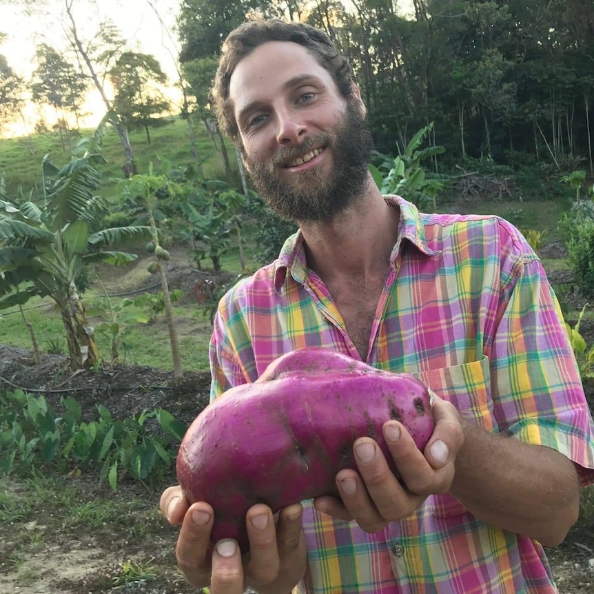 A bearded man smiles as he holds a purple-coloured vegetable.