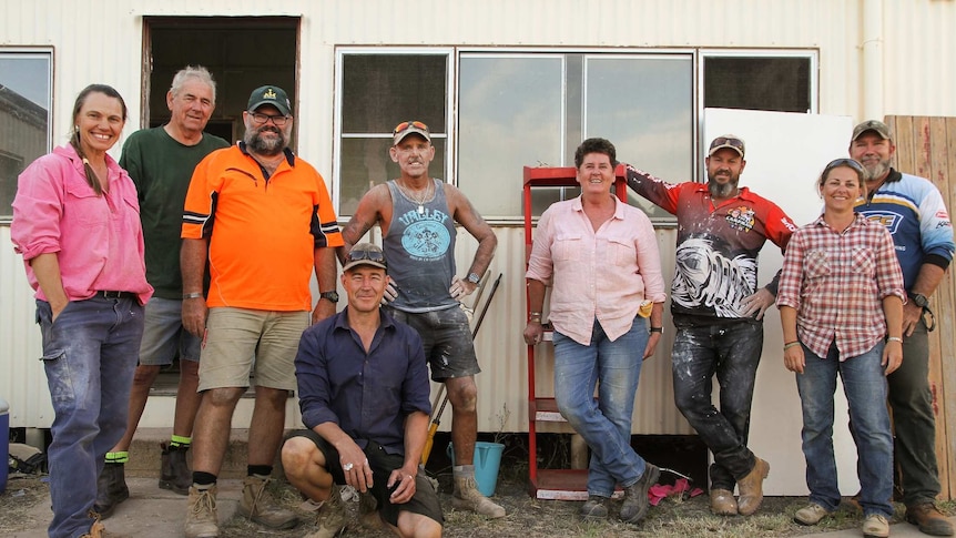 Men and women in work clothes stand smiling outside a shed.