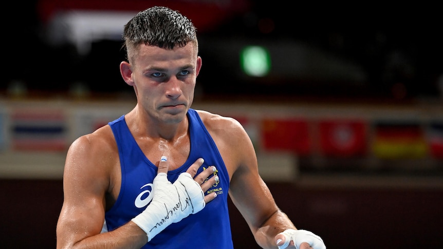 Harry Garside wearing a blue singlet puts his hand on his heart after winning a fight.