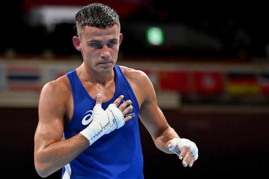 Harry Garside wearing a blue singlet puts his hand on his heart after winning a fight.