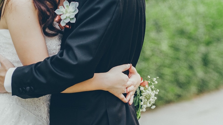 Bride and groom stand in front of greenery