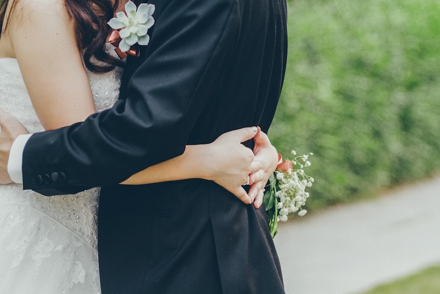 Bride and groom stand in front of greenery