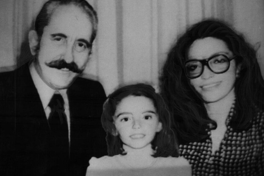 A black and white photo of a little girl sitting between a mustached man and a woman with thick glasses 