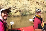 Two people sit in a kayak on the Murray River in front of a cliff. 