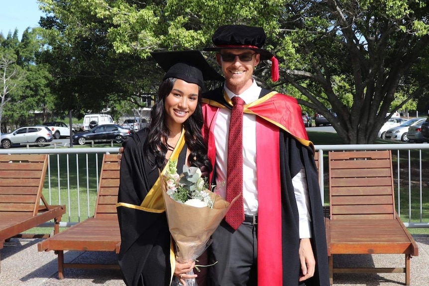 Student Veronica McNevin in graduation robe and holding flowers alongside mentor Dr Adrian Gepp