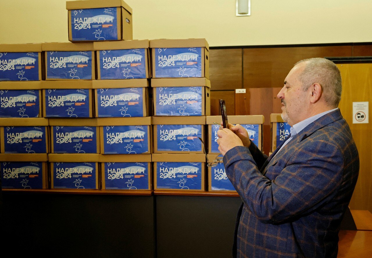 A man staning near a large pile of boxes, looking at his mobile phone