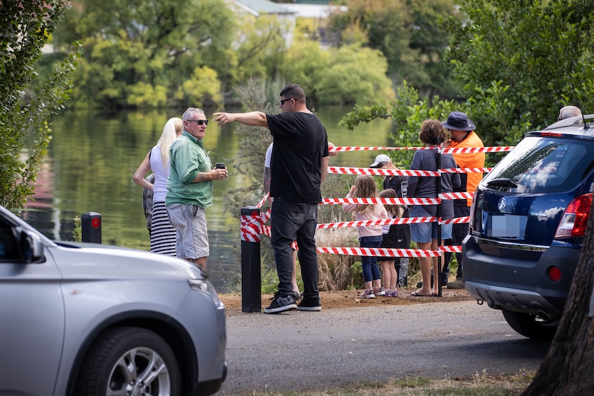 People stand near taped off poles at the edge of the water.