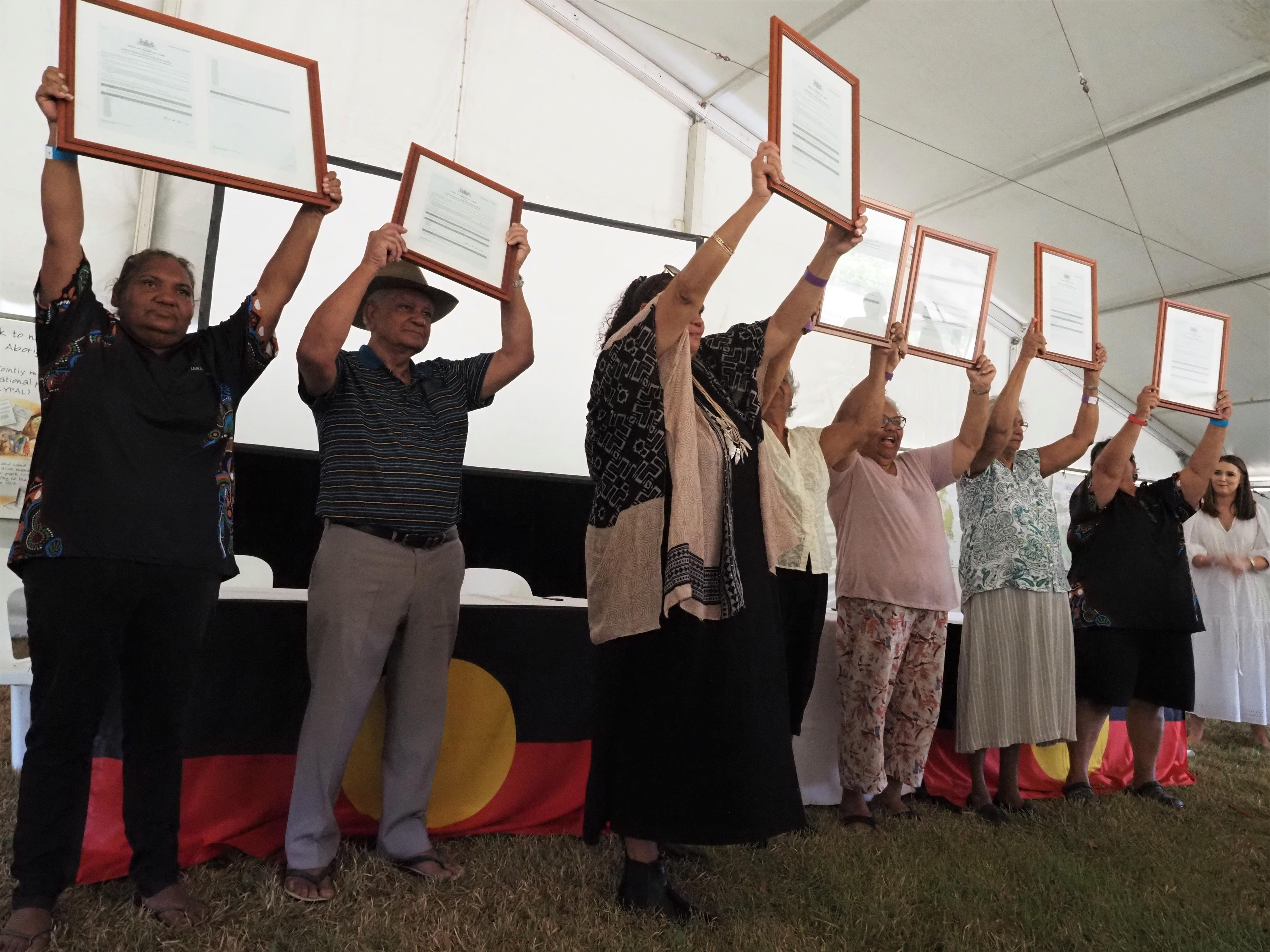 Indigenous people in a line hold up land deeds.