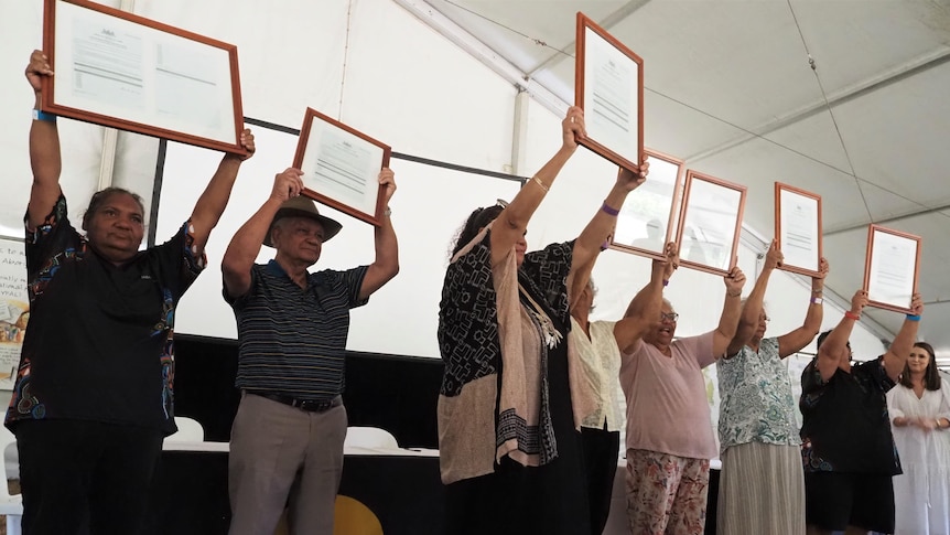 Indigenous people in a line hold up land deeds.