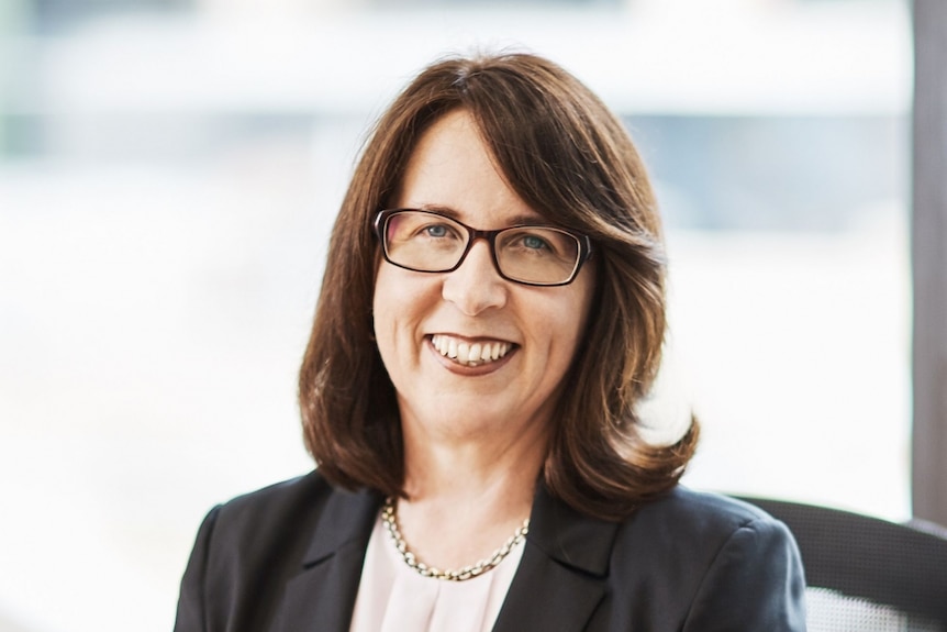 Angelene Falk sitting, wearing a suit and smiling.