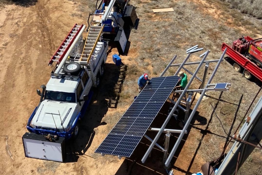 White ute with equipment on it is parked next to a solar panel which two men are working on