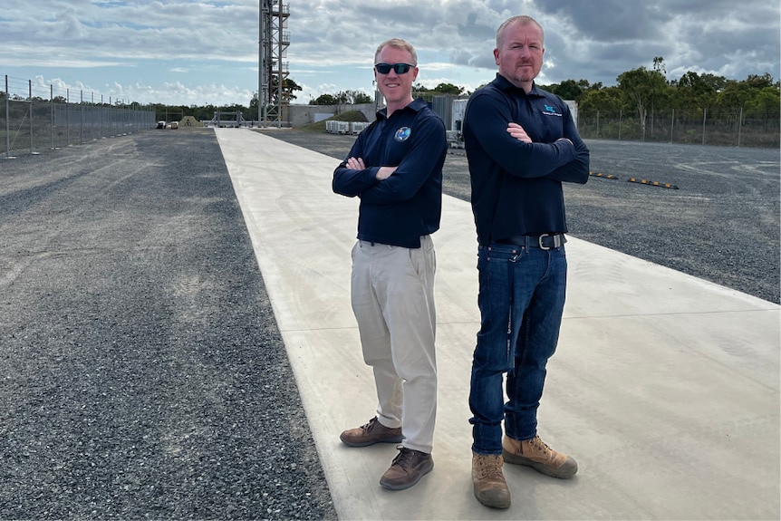 Two men stand with arms crossed on rocket launch pad