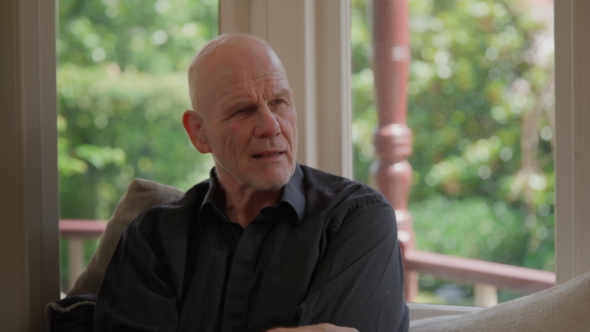 Peter sits in front of a large window while talking to someone off-screen.
