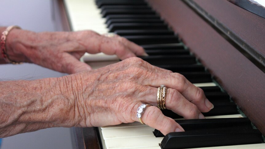 An older woman's hands resting on piano keys.