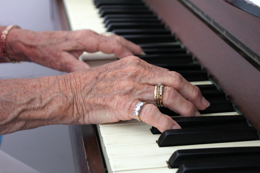 An older woman's hands resting on piano keys.