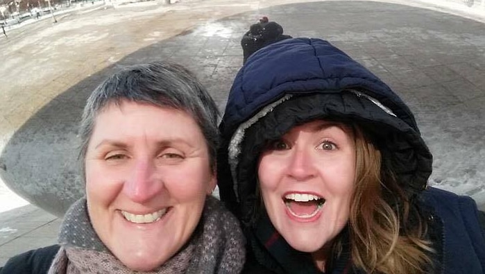 Two women smiling a cold winter day, with snow in the background.