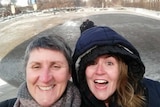 Two women smiling a cold winter day, with snow in the background.