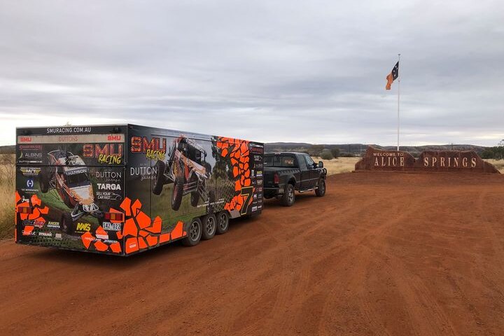 Ute with brightly coloured trailer in front of red Alice Springs welcome sign