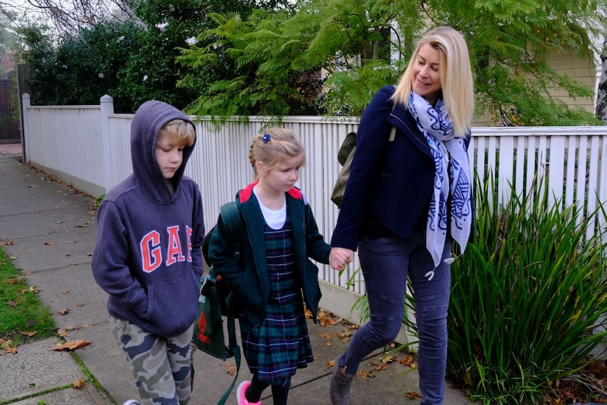 A blonde mum holds her young daughter's hand as she walks down the street alongside her slightly older brother.