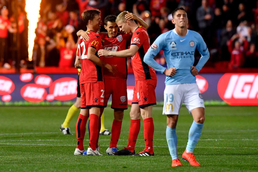 Lachlan Wales, right in a blue shirt, holds his hands on his hips as three players in red hug behind him and a flame lights up