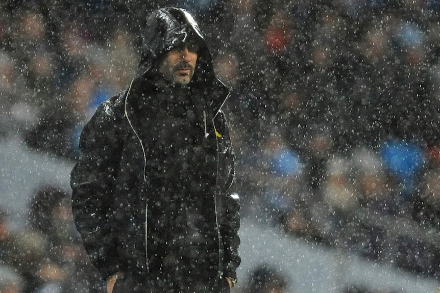 Pep Guardiola watches from the sideline in heavy rain as Manchester City plays Watford in the Premier League.