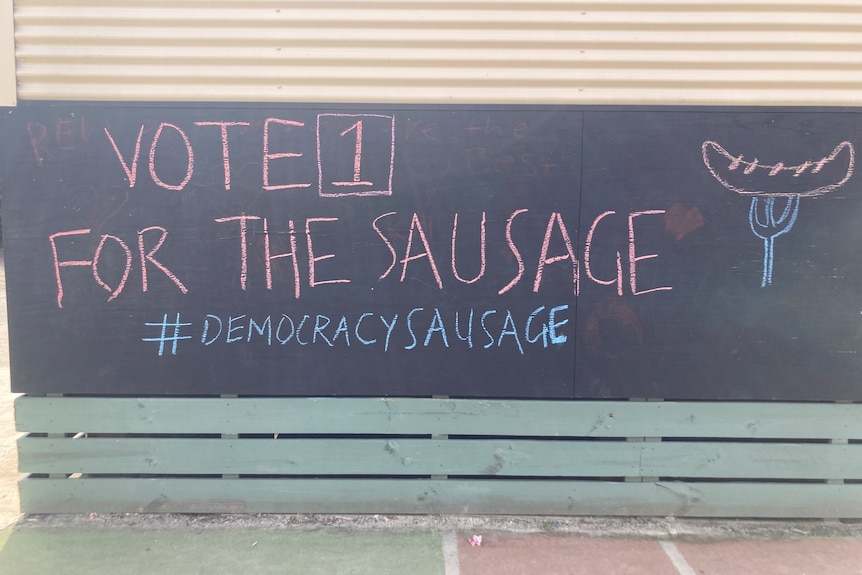A sign reading "vote 1 for the sausage #democracysausage" in chalk at a voting centre.