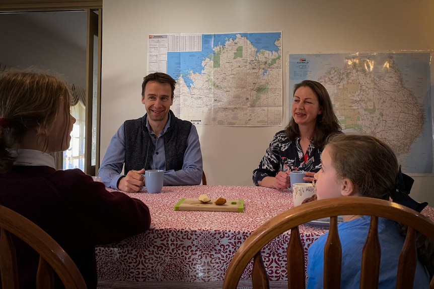 Une famille de quatre personnes assises avec des tasses de thé à une table avec une nappe à carreaux rouges et blancs.