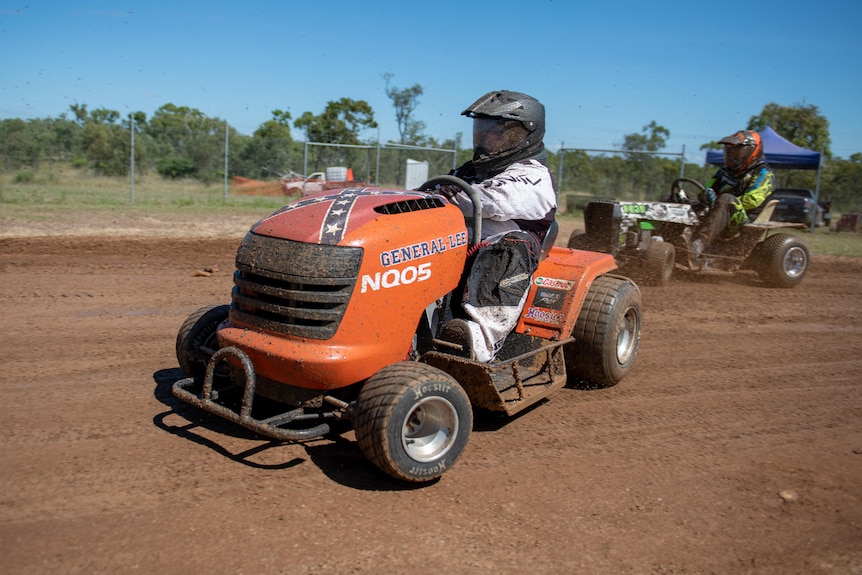 A man sits on an orange ride-on mower emblazoned with the confederate flag