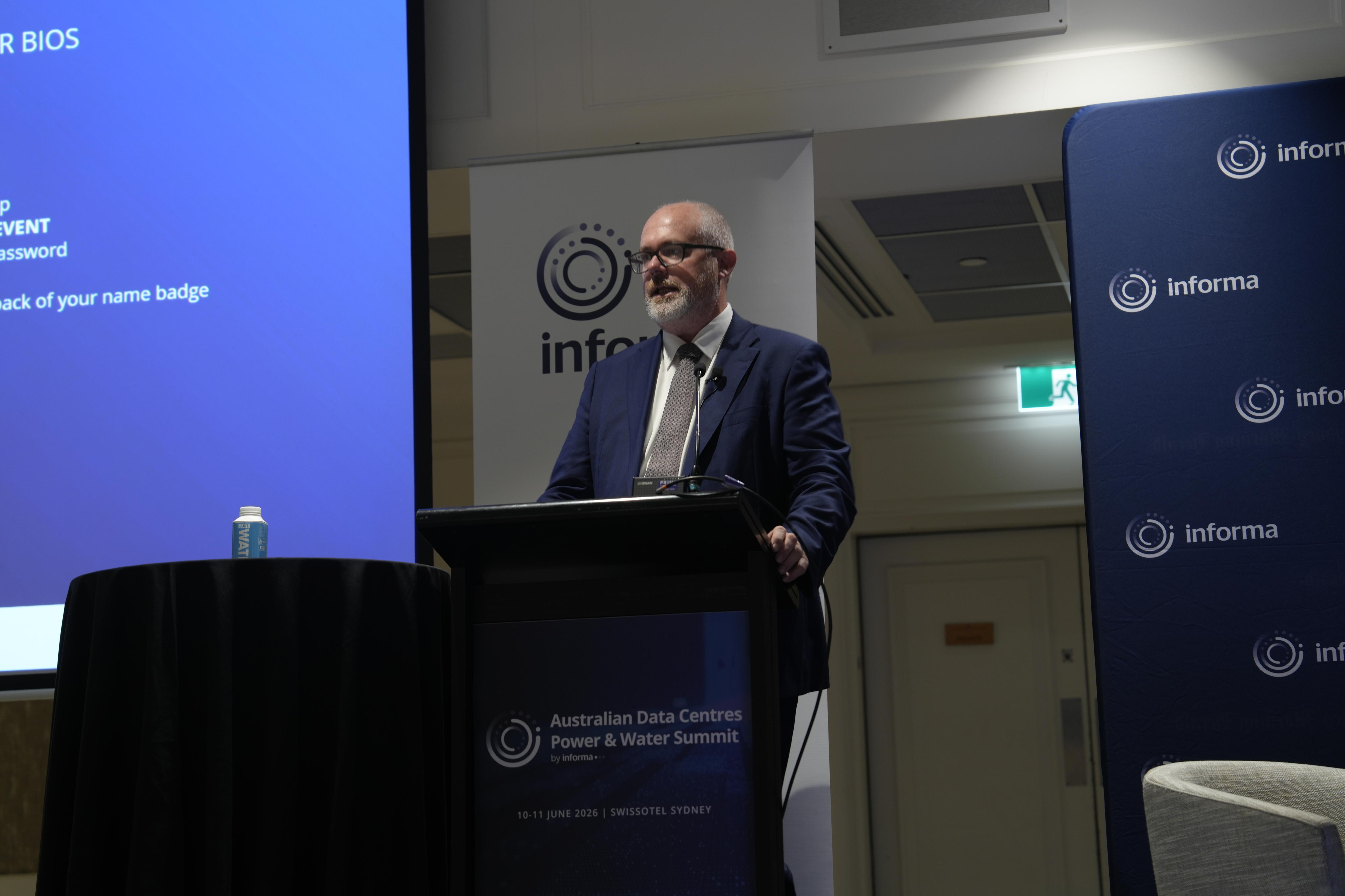 A man wearing a suit speaks at a lecturn.