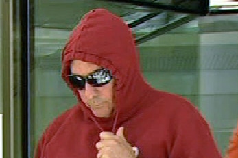 A man in a hoodie and sunglasses exits a court building.