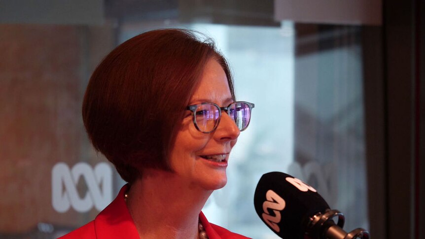 Julia Gillard smiles as she speaks into an ABC-branded microphone inside a radio studio.