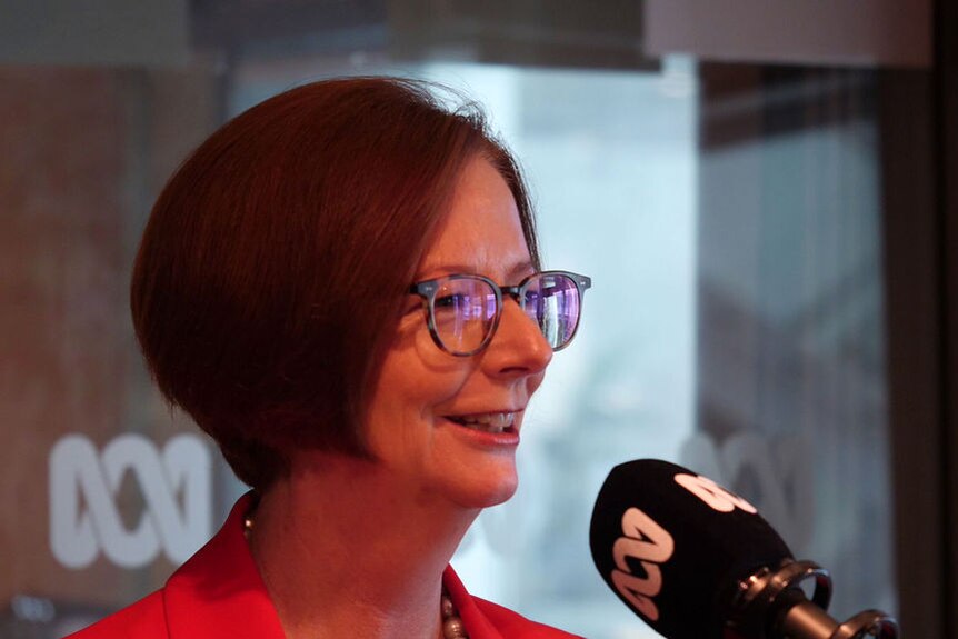 Julia Gillard smiles as she speaks into an ABC-branded microphone inside a radio studio.