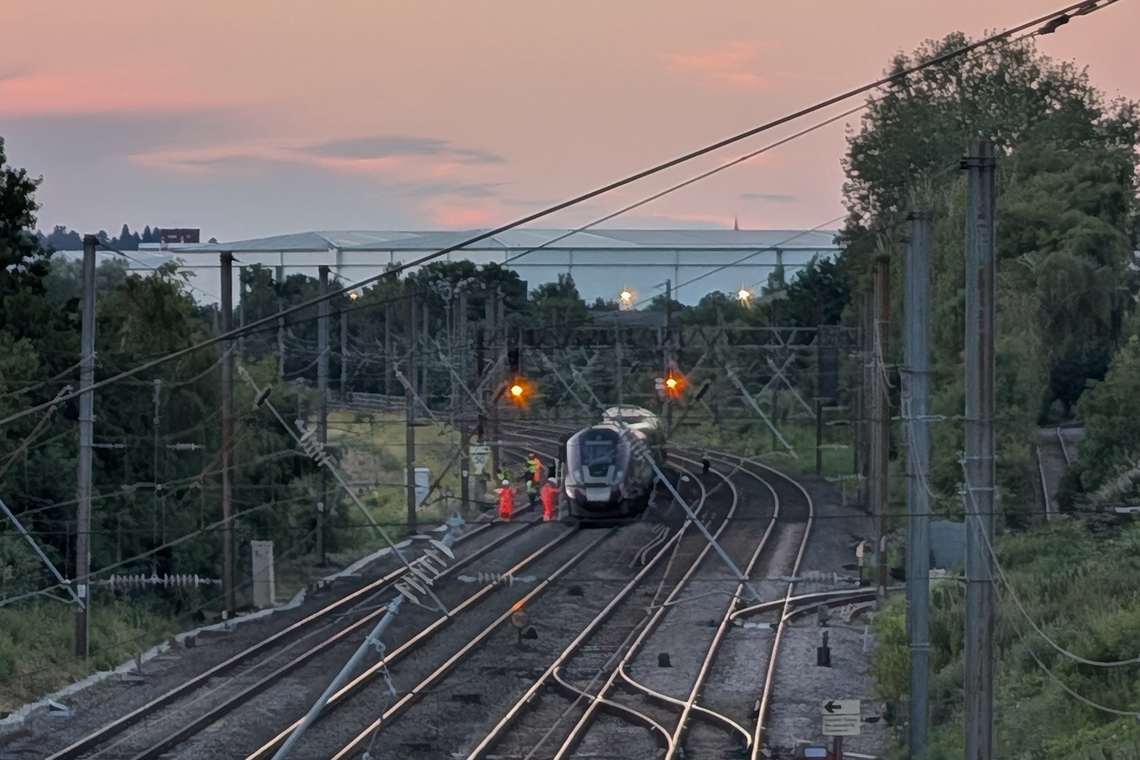 a wide shot of a train stopped on tracks as high-vis crew attend and the sun sets
