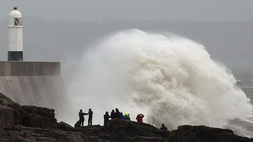 People stand on the rocks as large waves break against barriers at the harbour in Porthcawl