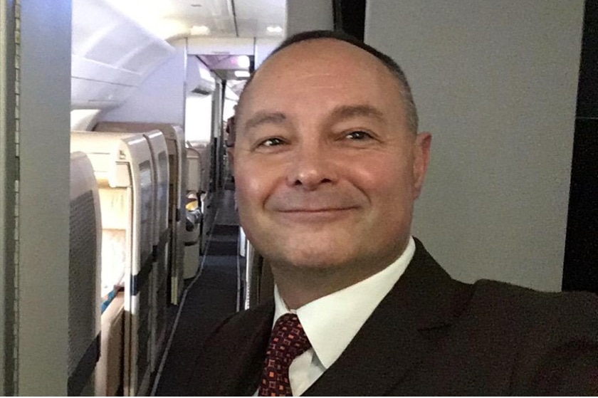 A male air cabin crew member stands in the hallway inside a plane.