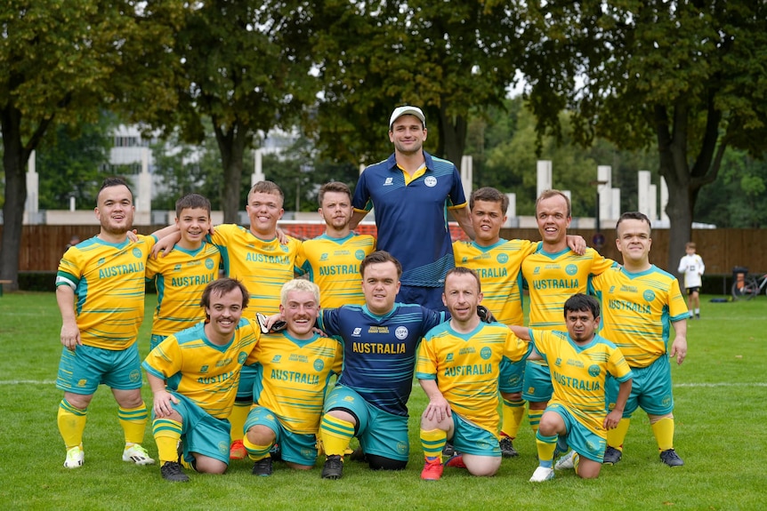 The Australian Men's Football Team, wearing green and gold uniforms, pose for a team photo.