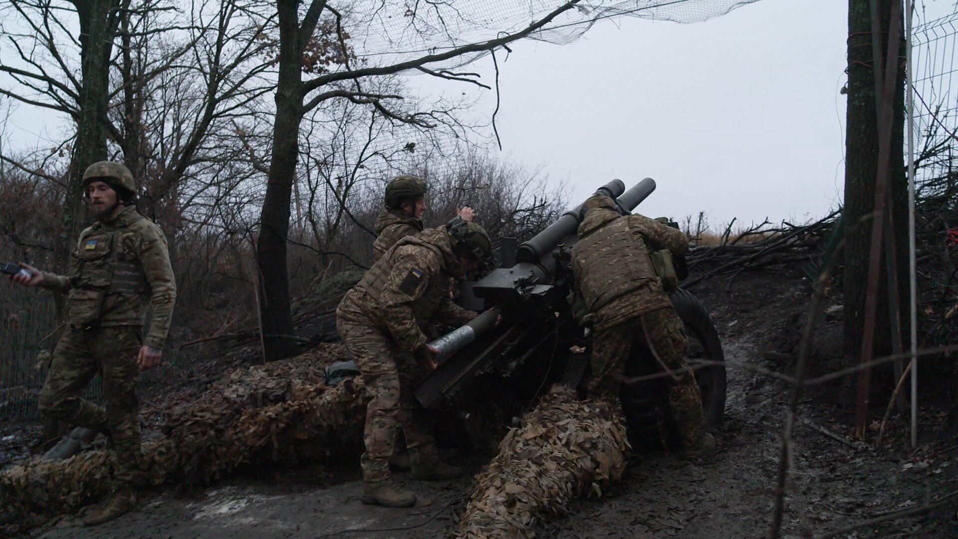 Five soldiers stand behind a heavy artillery weapon, one is loading a shell.