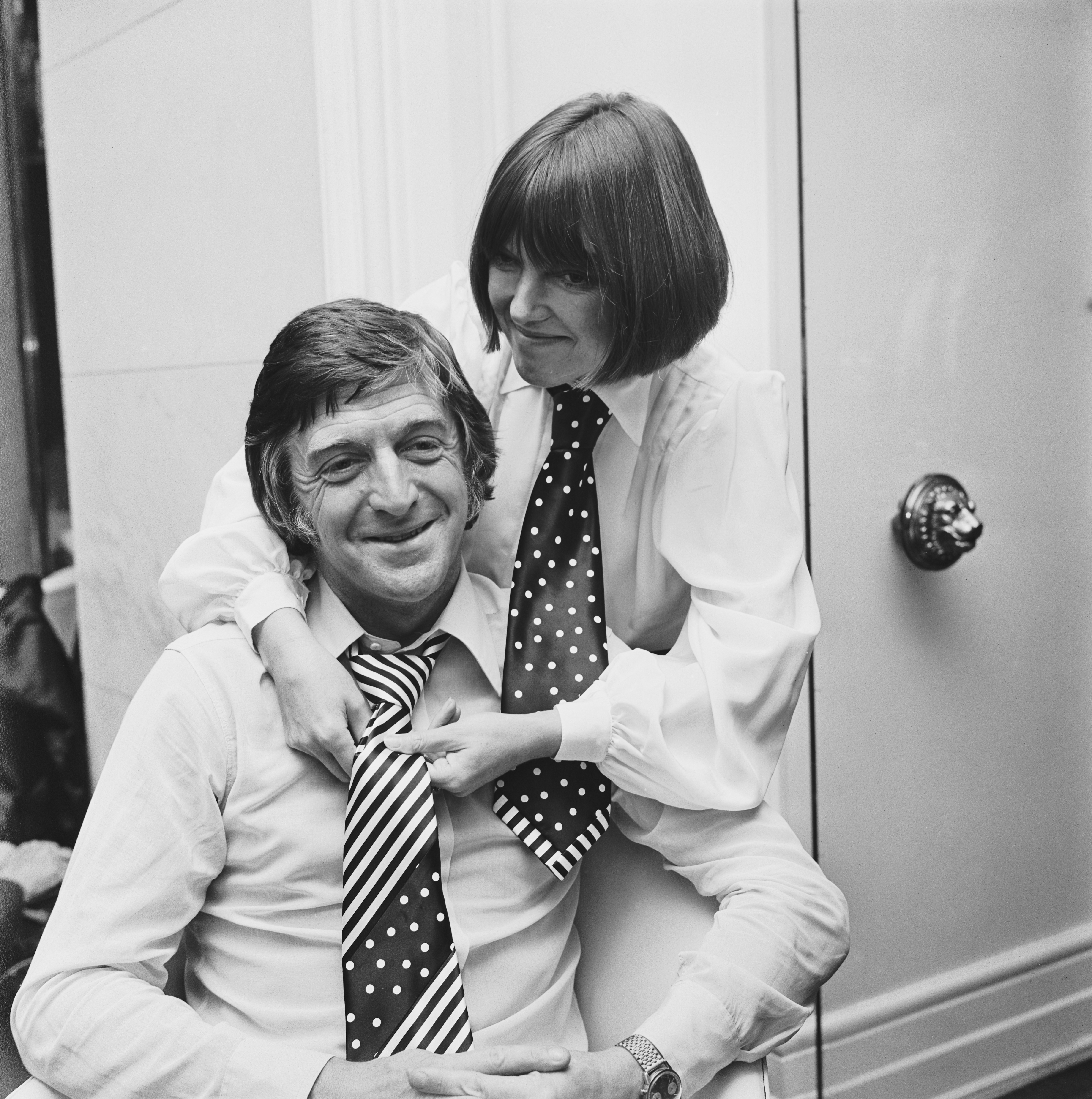 Mary Quant adjusts a polka dot striped necktie on English broadcaster, journalist and author Michael Parkinson