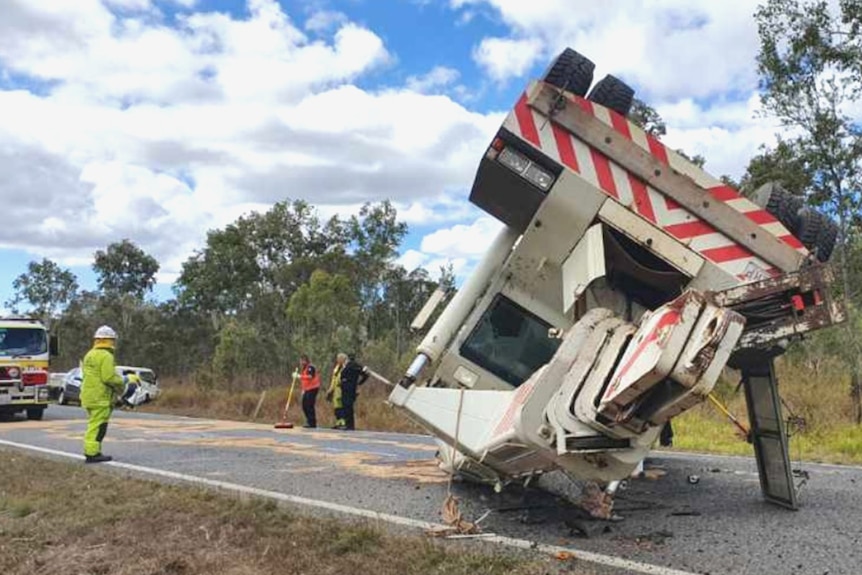 A large crane truck overturned in the middle of a country road