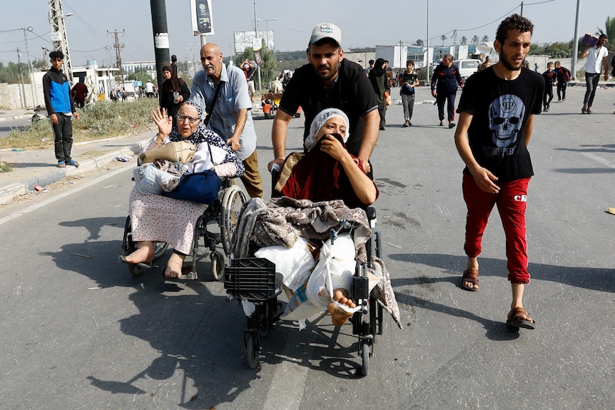 injured women in wheelchairs being pushed along on road