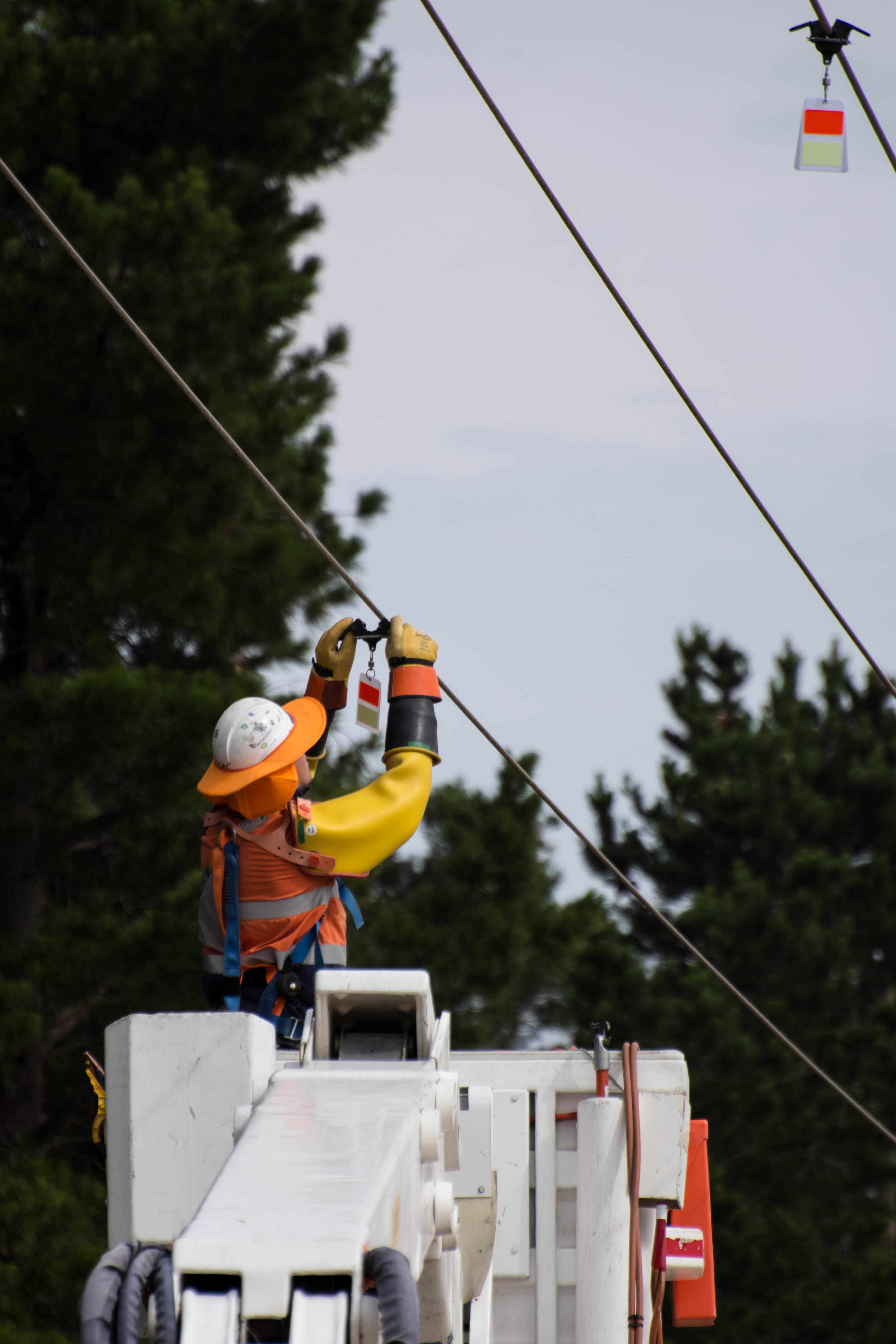A worker in a safety helmet and vest uses equipment to manage overhead wires from an elevated platform.