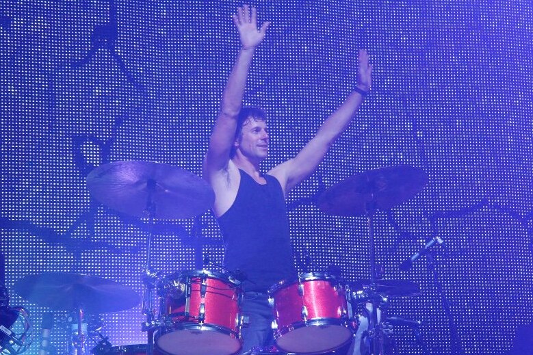 Powderfinger drummer Jon Coghill stands behind a drum kit, Jon changed careers later in life after a successful stint as a muso