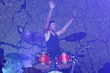 Powderfinger drummer Jon Coghill stands behind a drum kit, Jon changed careers later in life after a successful stint as a muso