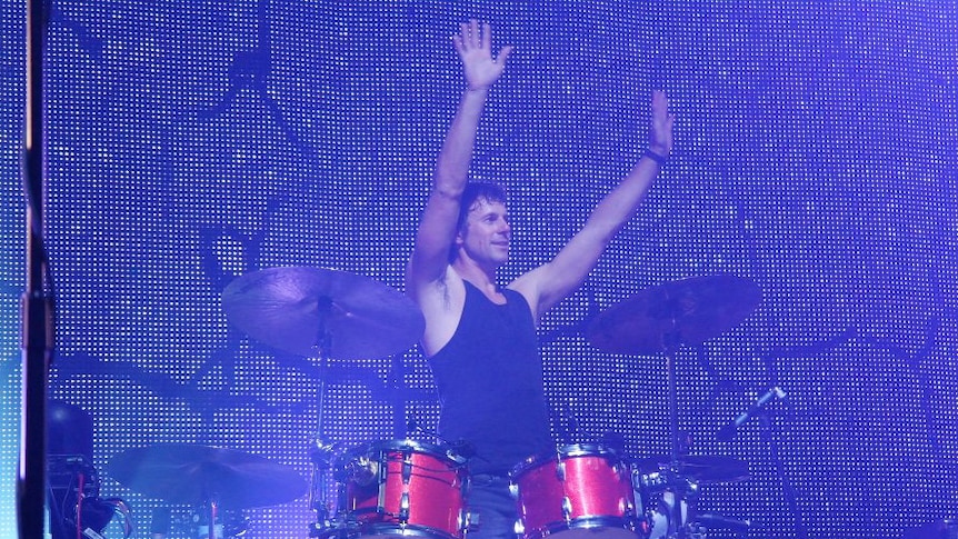 Powderfinger drummer Jon Coghill stands behind a drum kit, Jon changed careers later in life after a successful stint as a muso