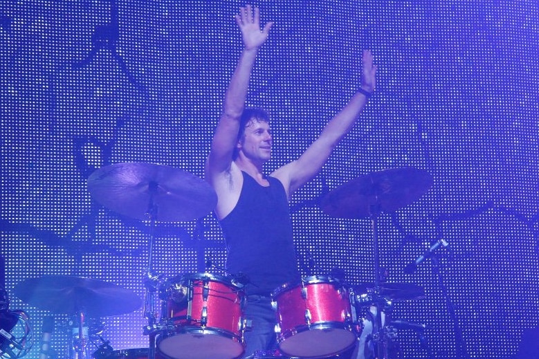 Powderfinger drummer Jon Coghill stands behind a drum kit, Jon changed careers later in life after a successful stint as a muso