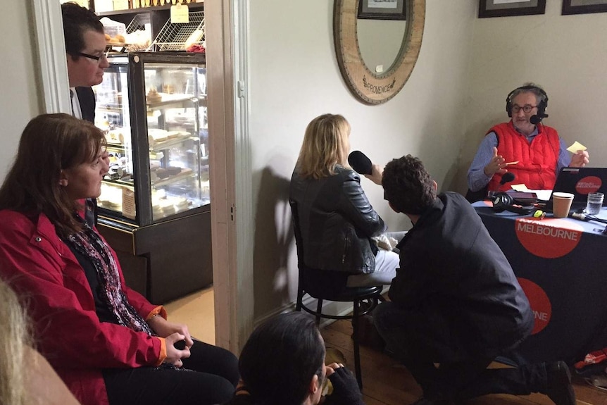 People watch a radio broadcast in a cafe.