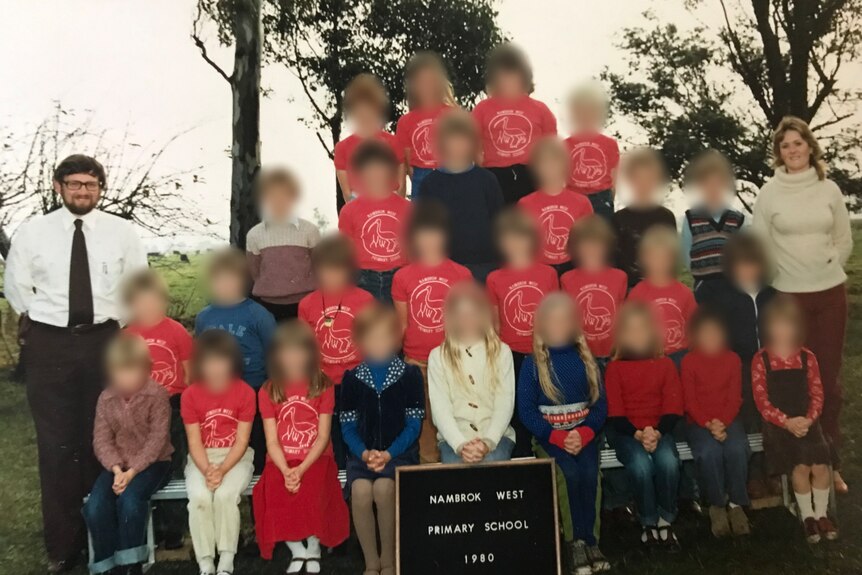  An old school photo with a male and female teacher. The faces of children are blurred.